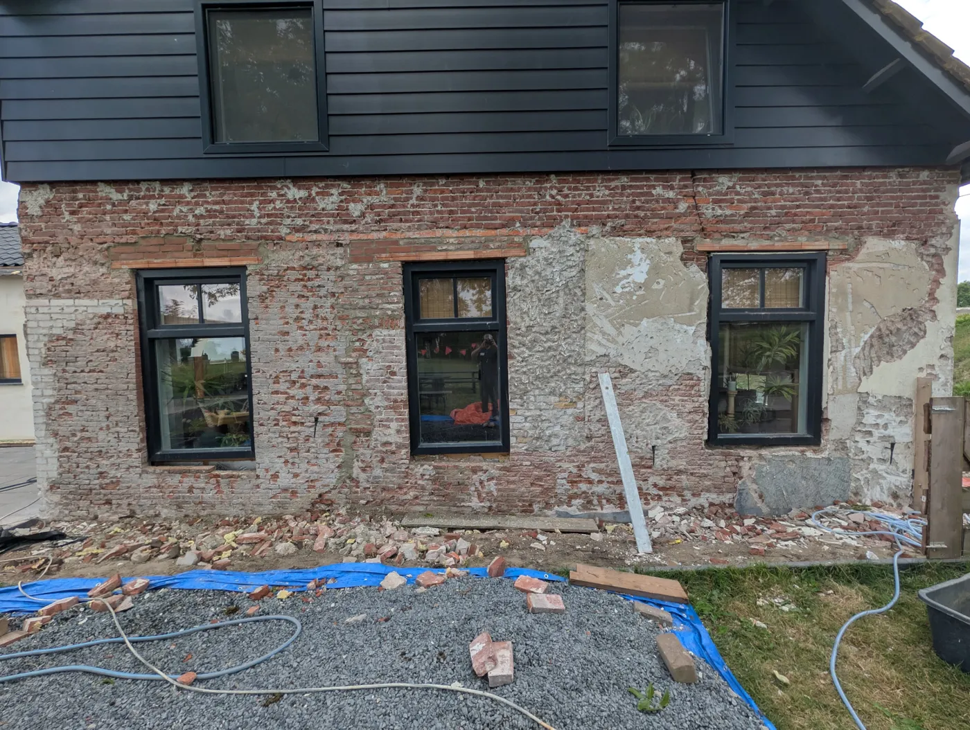 Oude gevel waar de pleister vanaf is gehaald, met baksteen en cementreparaties