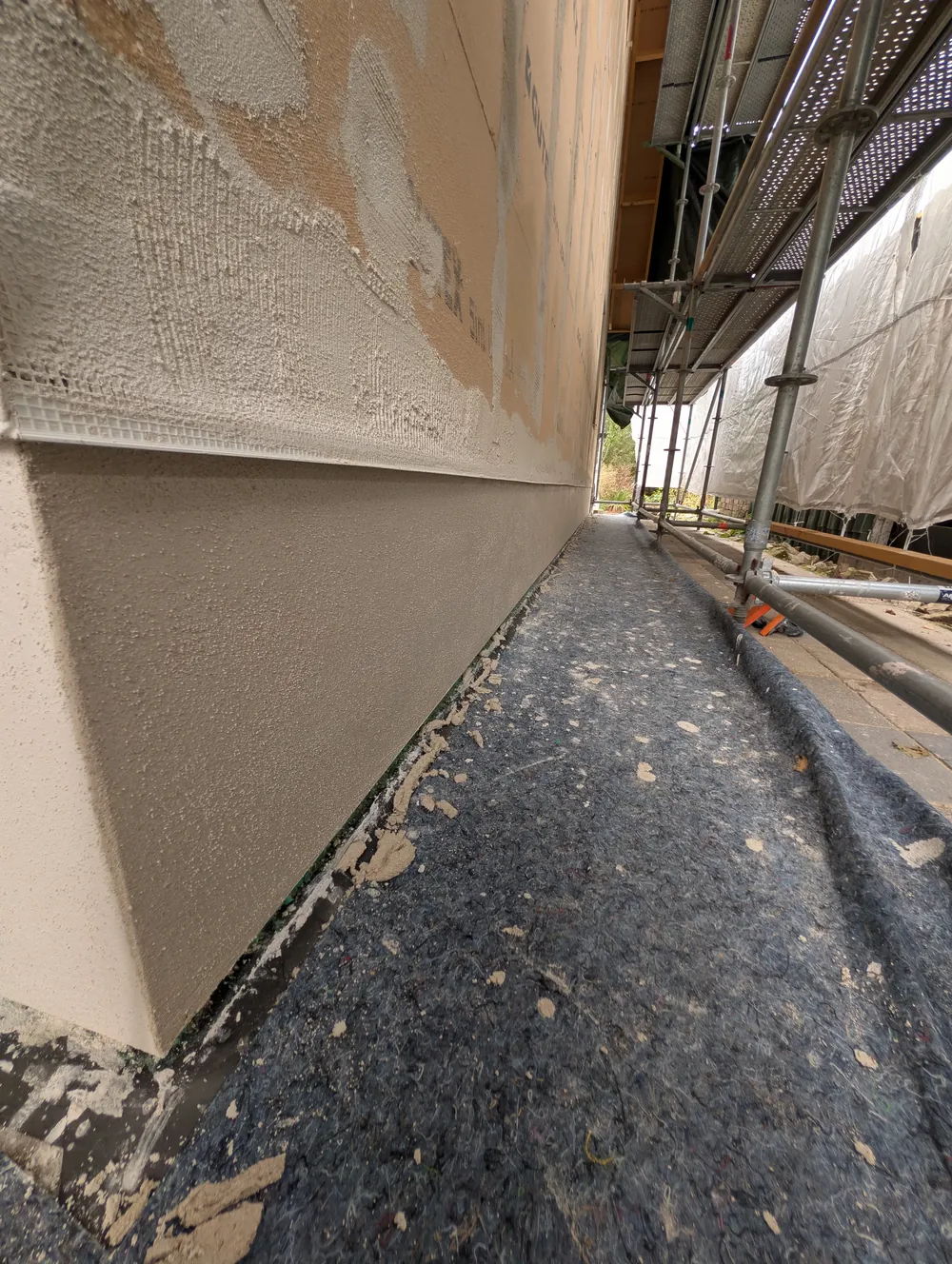 Onderaan de gestucte kalkplint, daarboven het sokkelprofiel. Het gaas van het profiel is al vastgezet op de houtvezelplaat. Daarna volgt de grondlaag met wapening over de hele gevel.